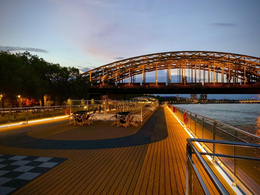 Cubierta de un barco fluvial al anochecer, junto a un puente iluminado
